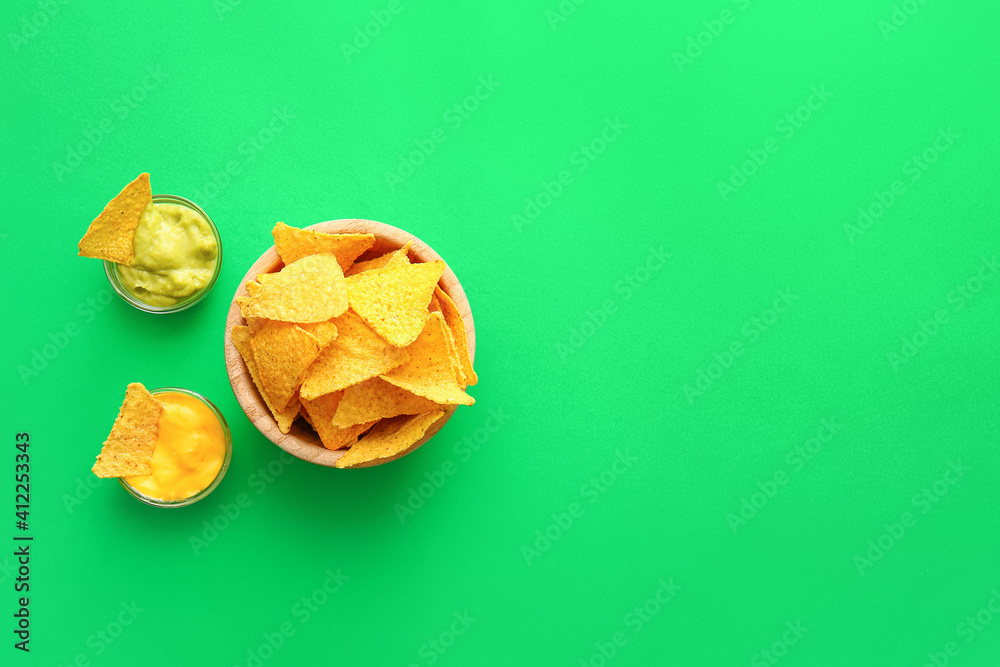 Bowl with tasty nachos and sauces on color background