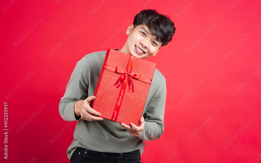 Young man holding gift box on red background