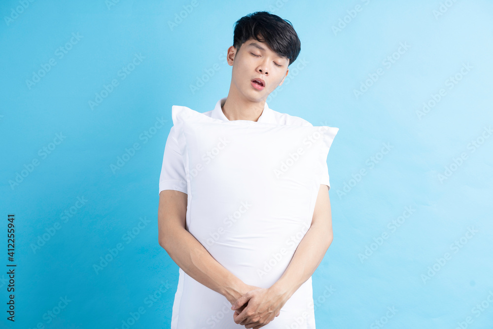 Portrait of young man holding sleepy pillow on blue background