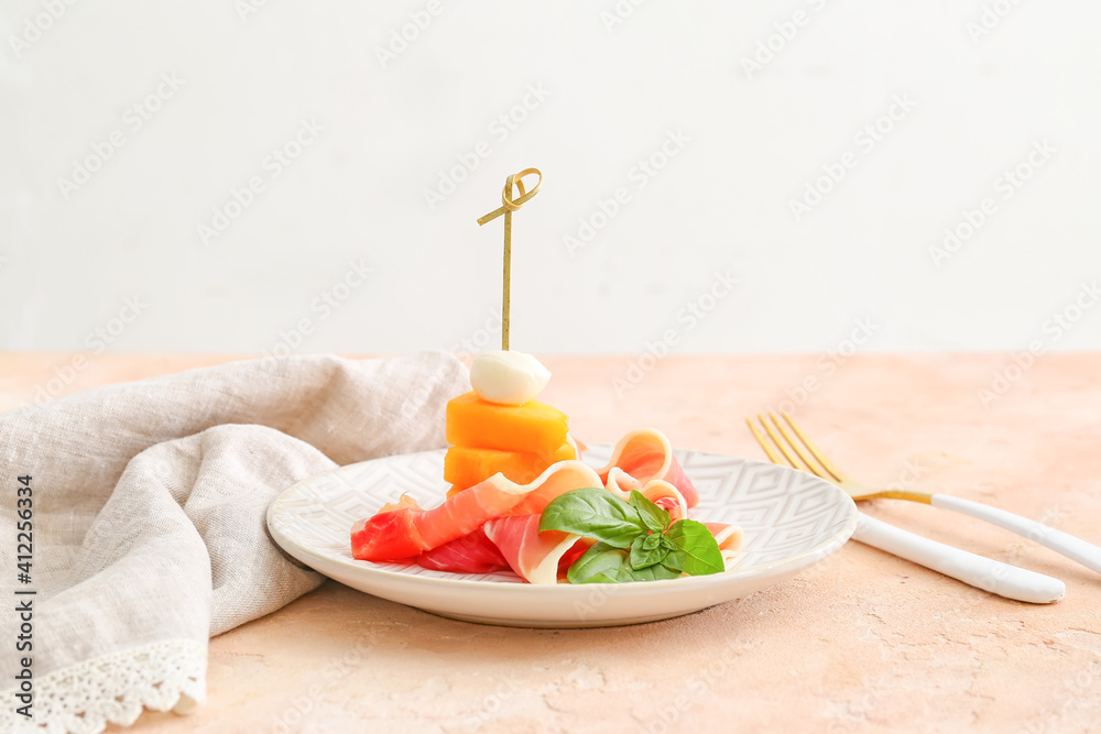 Plate with delicious melon, mozzarella and prosciutto on color background