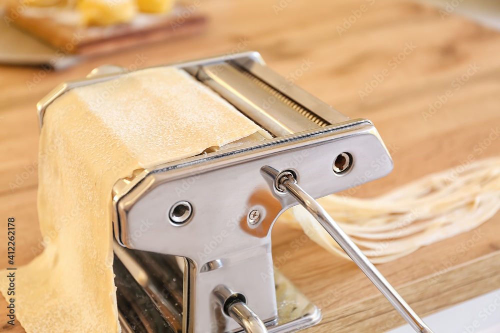 Pasta maker with dough on table in kitchen