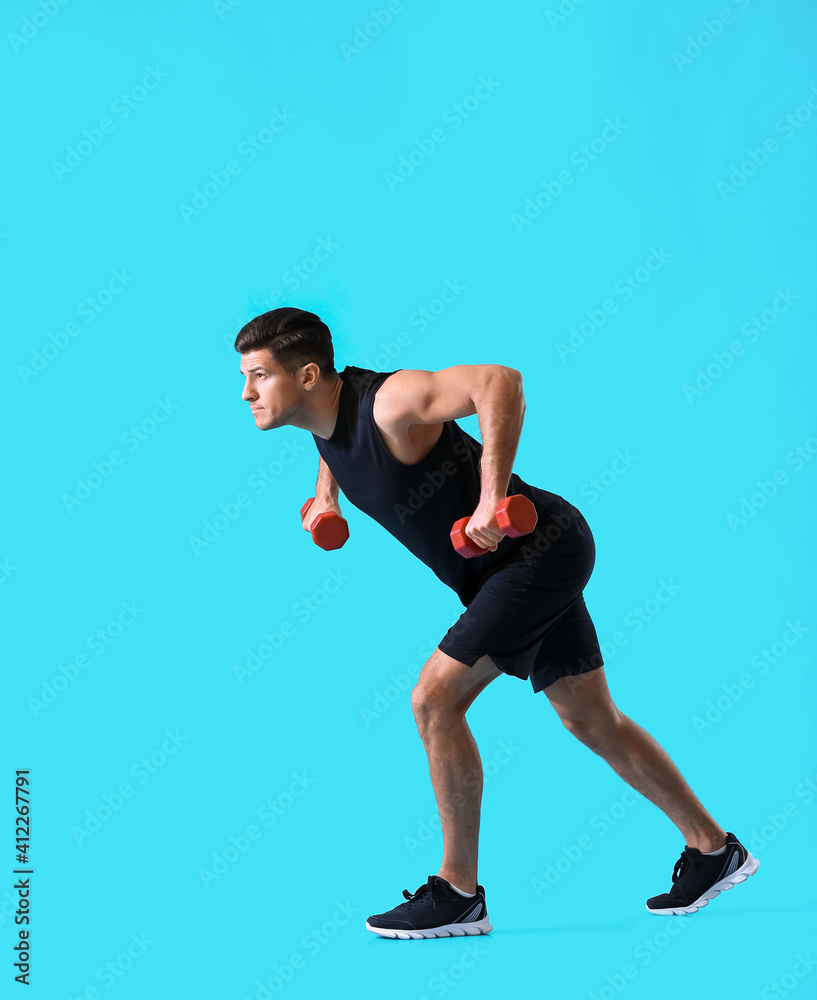 Sporty young man training with dumbbells on color background