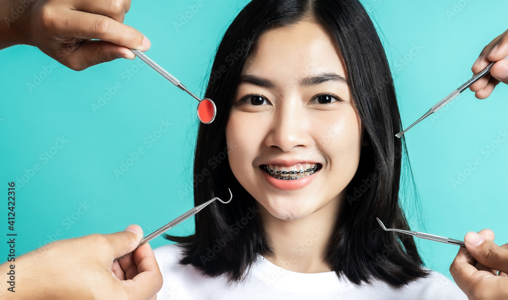 Asian woman wearing dental braces pointing to tooth sample and smiling with her healthy white teeth 