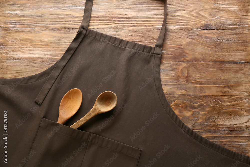 Clean apron and spoons on wooden background, closeup