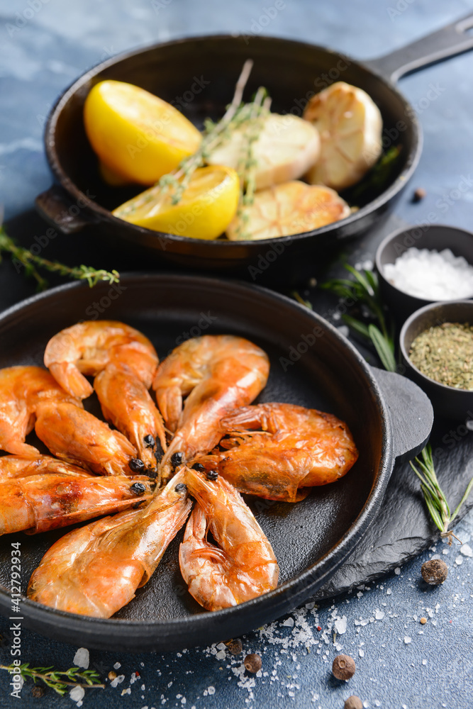 Frying pans with tasty shrimps, garlic and lemons on color background