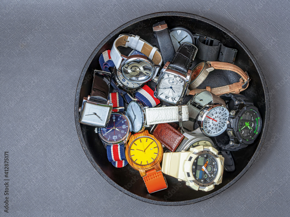 A pile of wristwatches on a black plate over a dark background.