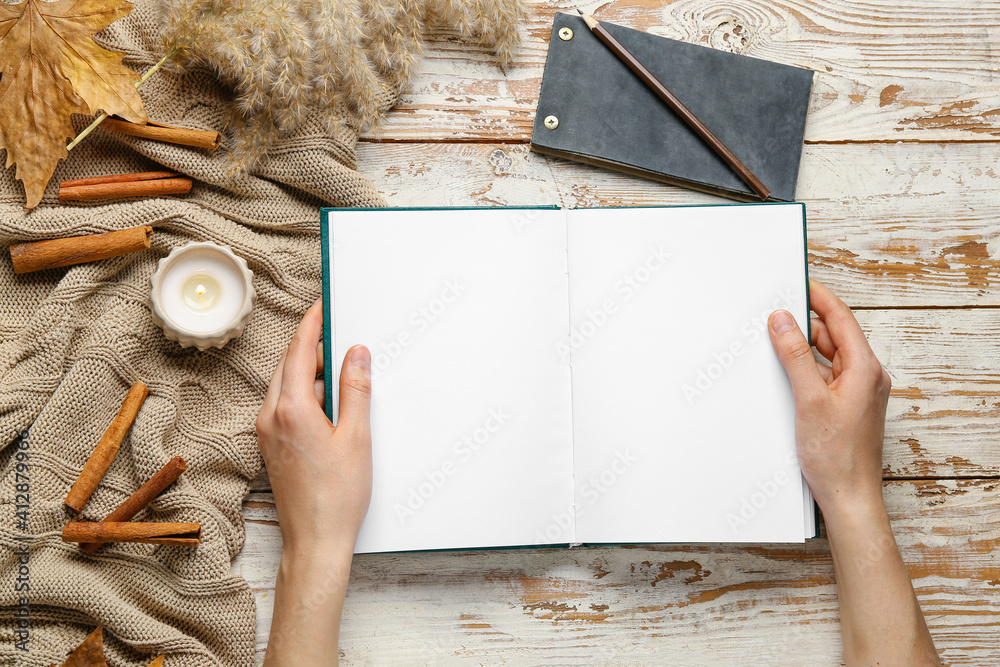 Female hands with blank open book, cinnamon and candle on wooden background