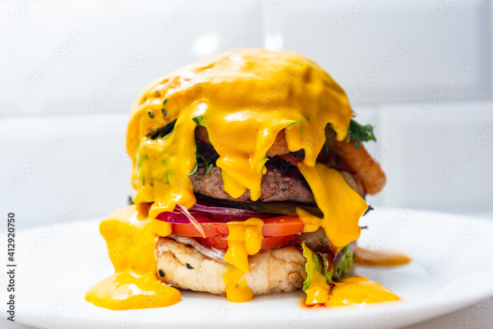 Fresh hamburger covered with melted cheese with grilled beef and onion rings on the plate