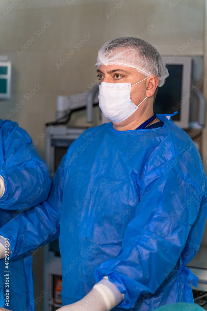 Serious doctor in scrubs looks attentively at working process in operation room. Medic in scrubs and