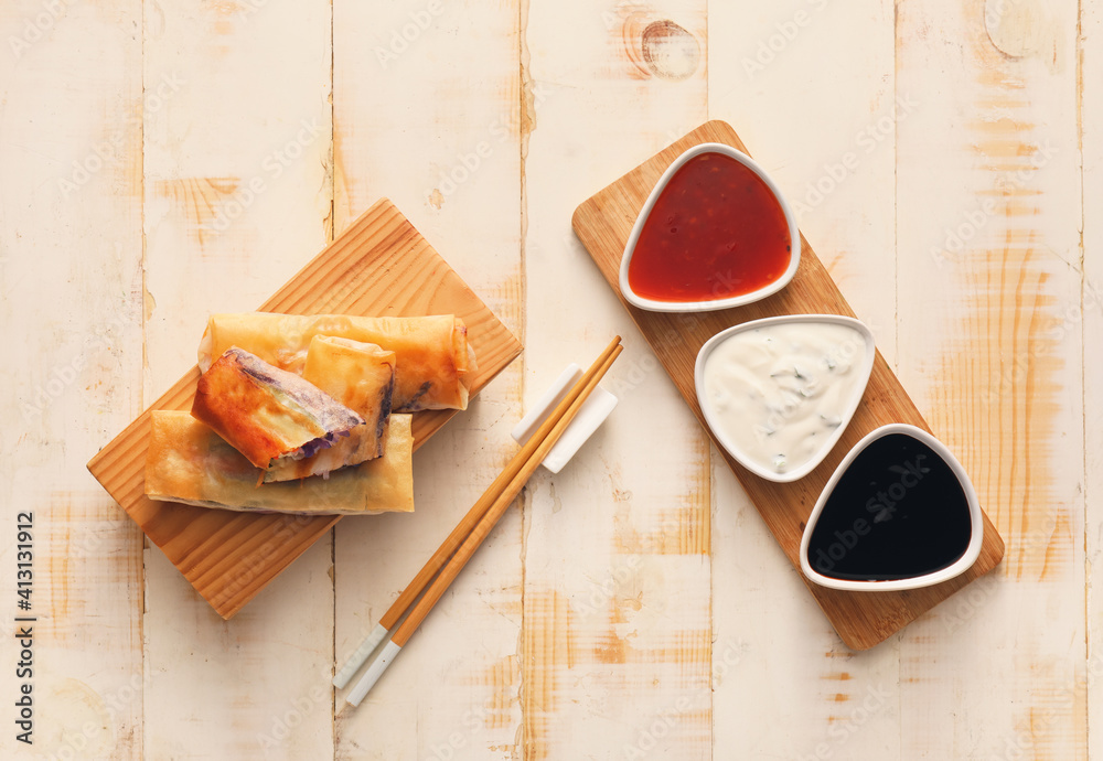 Boards with tasty fried spring rolls and sauces on wooden background