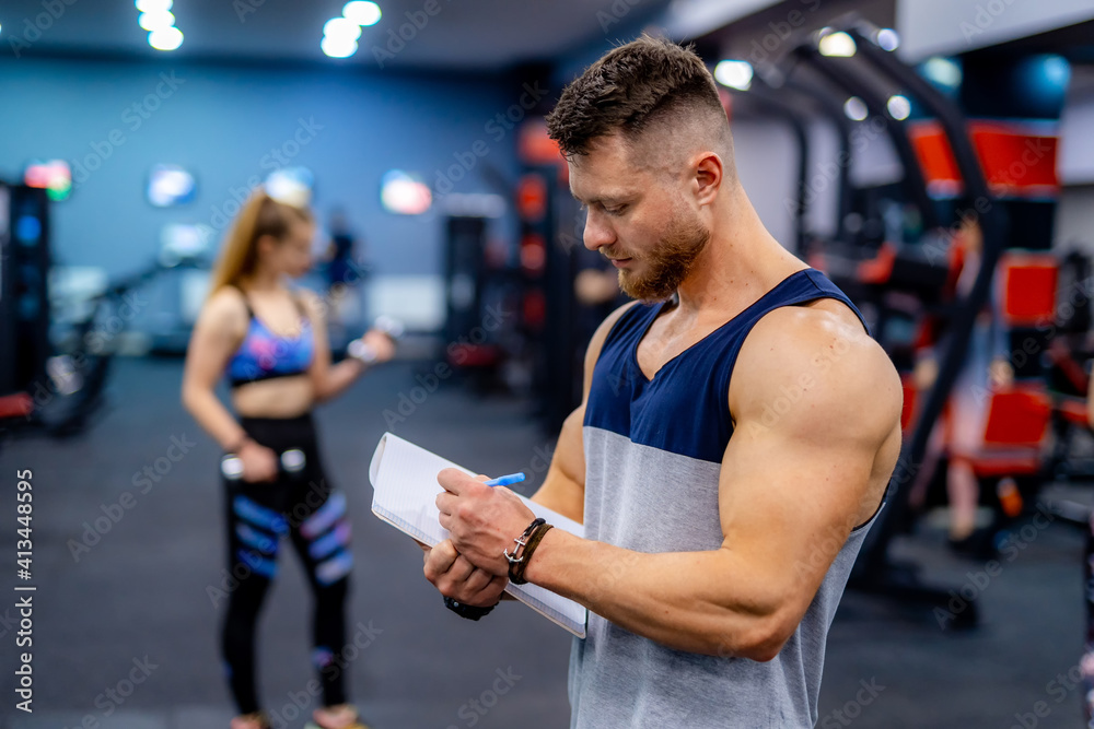 Handsome personal trainer with a clipboard in fitness center. Fitness instructor takes notes. Closeu