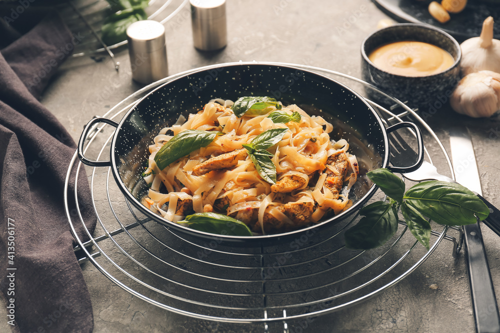 Frying pan with tasty noodles and chicken on table