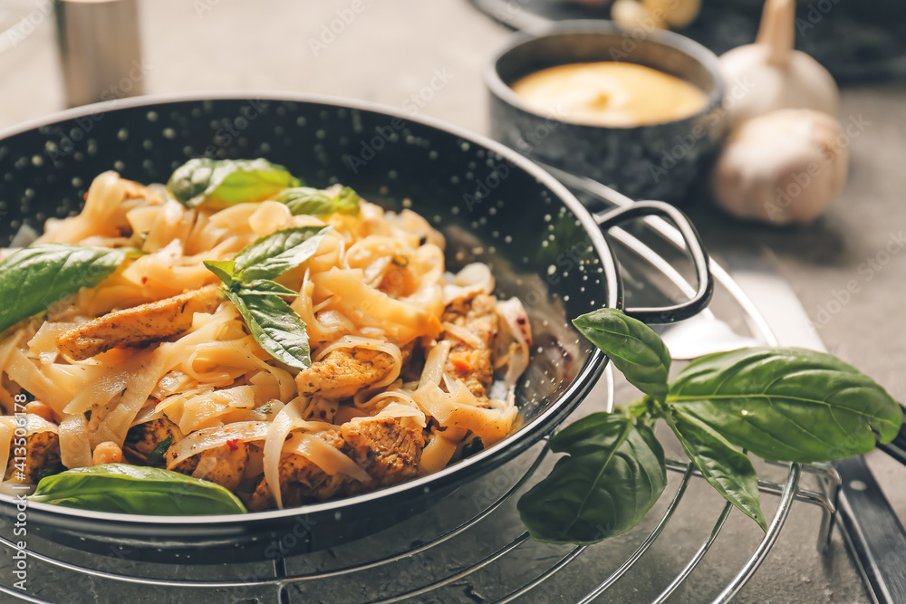 Frying pan with tasty noodles and chicken on table, closeup