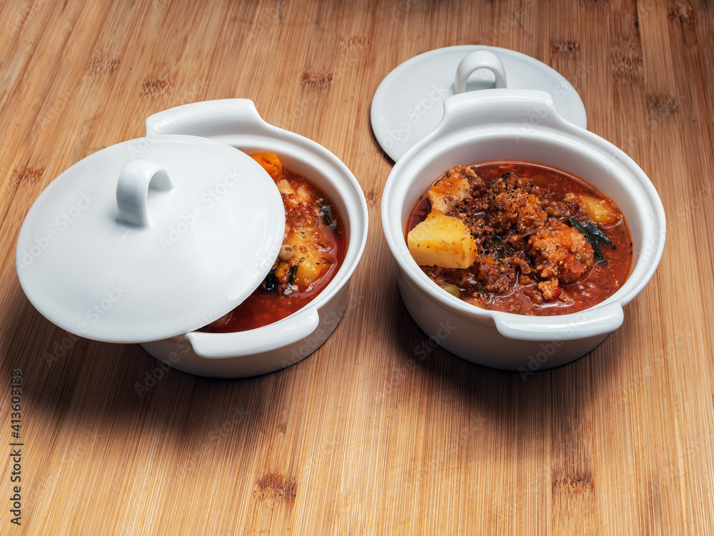 Two pots full of homemade stewed vegetables ragout with mushrooms and meatballs on the wooden table.