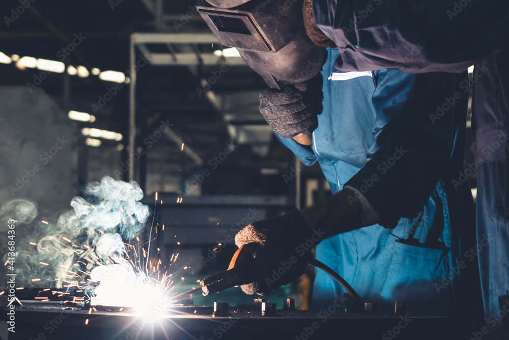 Skillful metal worker working with arc welding machine in factory while wearing safety equipment. Me