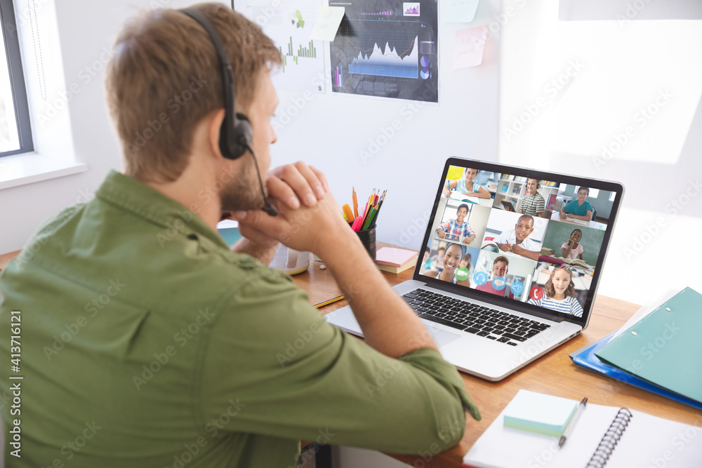 Male teacher wearing headphones having a video conference with multiple students on laptop at school