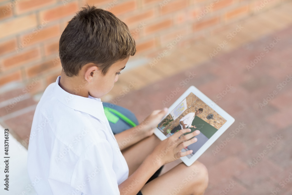 Male caucasian student having a video call with male teacher on digital tablet at school