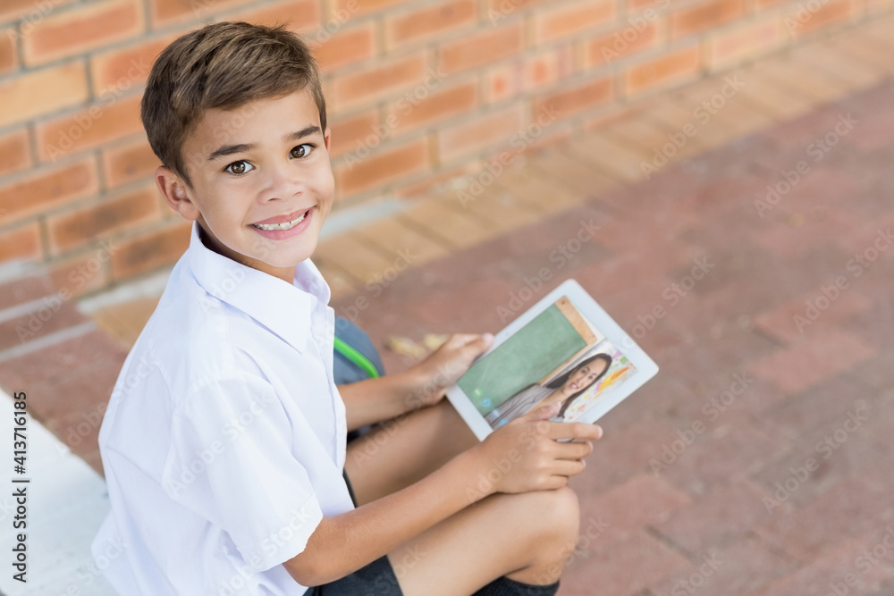 Portrait of male caucasian student having a video call with female teacher on digital tablet at scho