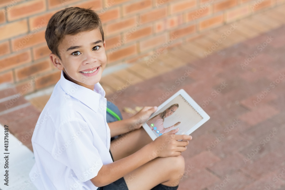 Portrait of male caucasian student having a video call with female teacher on digital tablet at scho