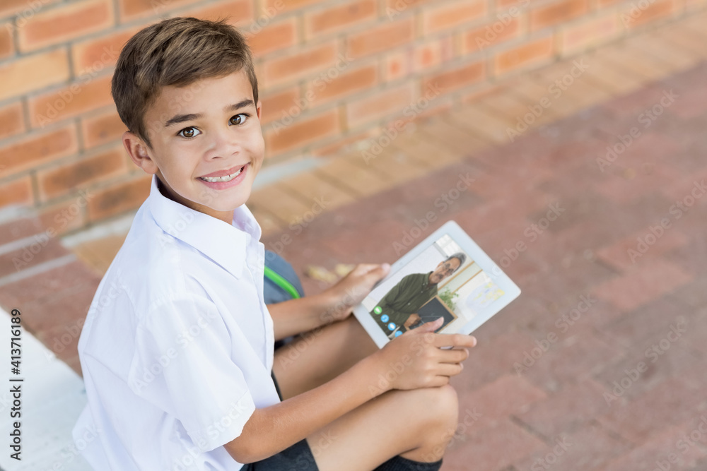 Portrait of male caucasian student having a video call with male teacher on digital tablet at school