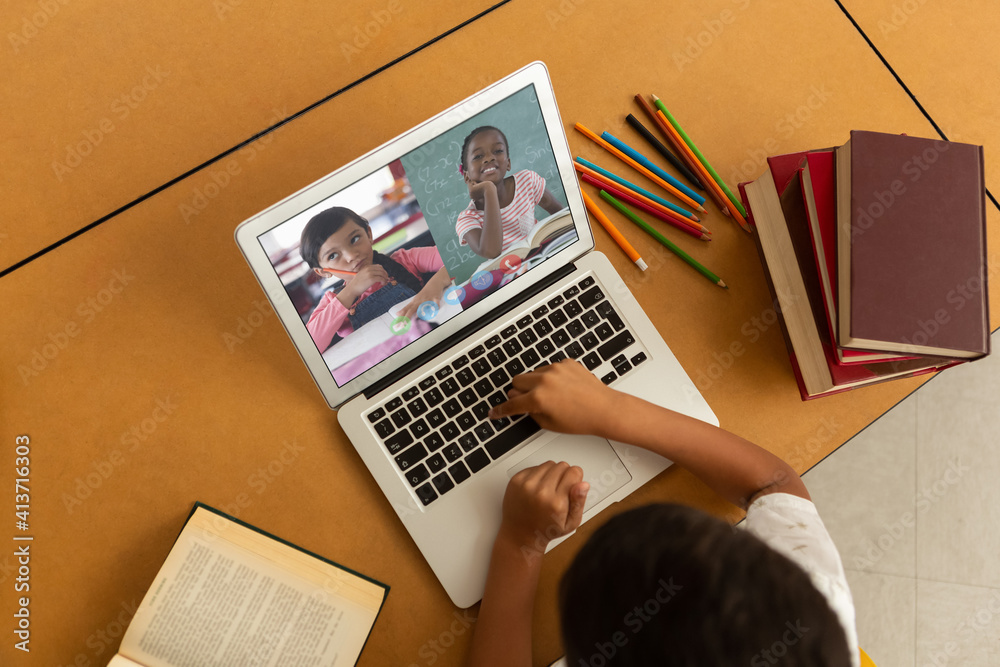 Overhead view of male student having a video conference with multiple students on laptop at school