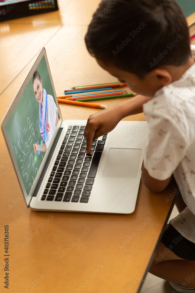 Male student having a video call with female teacher on laptop at school