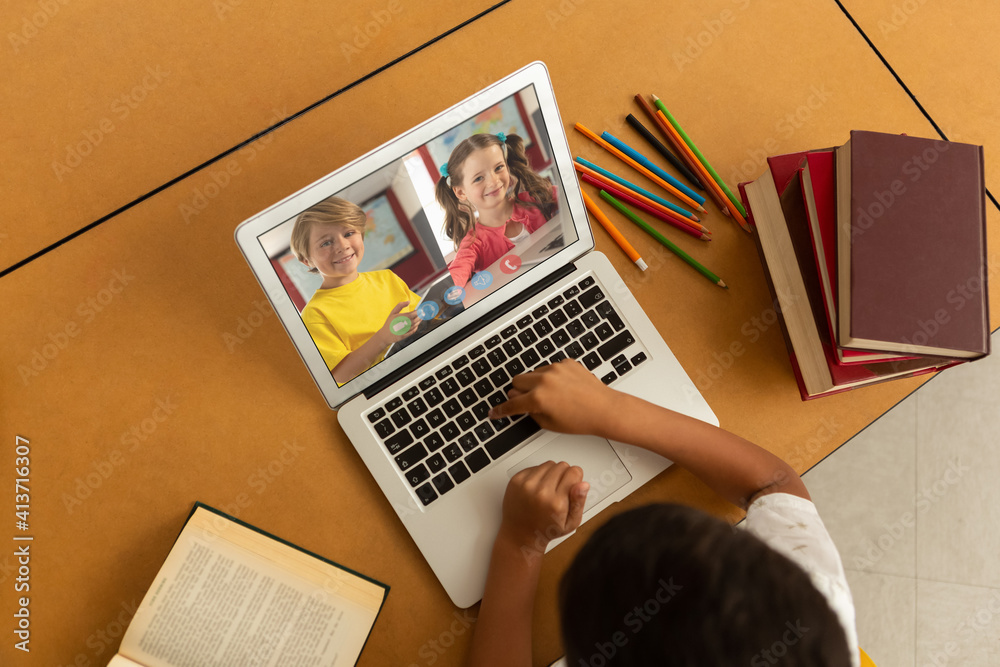 Overhead view of male student having a video conference with multiple students on laptop at school