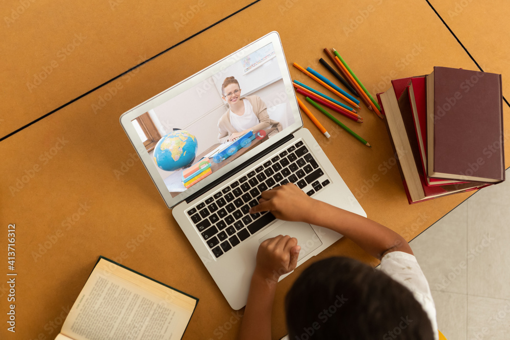 Overhead view of male student having a video call with female teacher on laptop at school