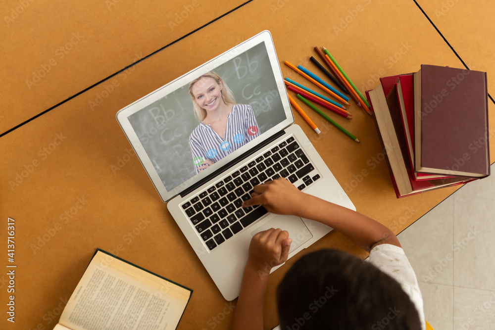 Overhead view of male student having a video call with female teacher on laptop at school