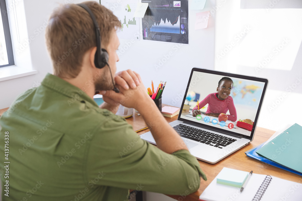 Male teacher wearing headphones having a video call with female student on laptop at school