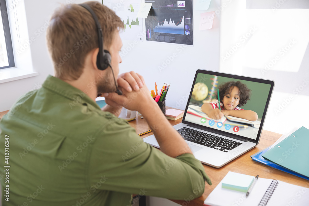 Male teacher wearing headphones having a video call with male student on laptop at school