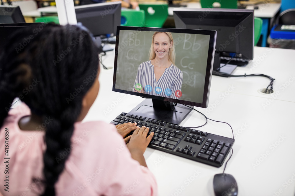 Female student having a video call with female teacher on computer at school