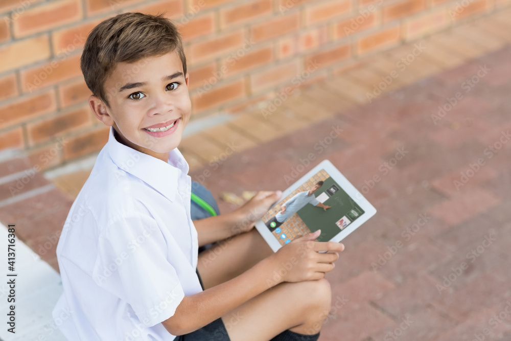 Portrait of male caucasian student having a video call with male teacher on digital tablet at school