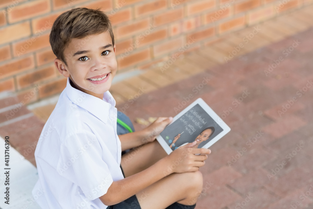 Portrait of male caucasian student having a video call with female teacher on digital tablet at scho