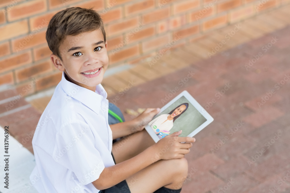 Portrait of male caucasian student having a video call with female teacher on digital tablet at scho