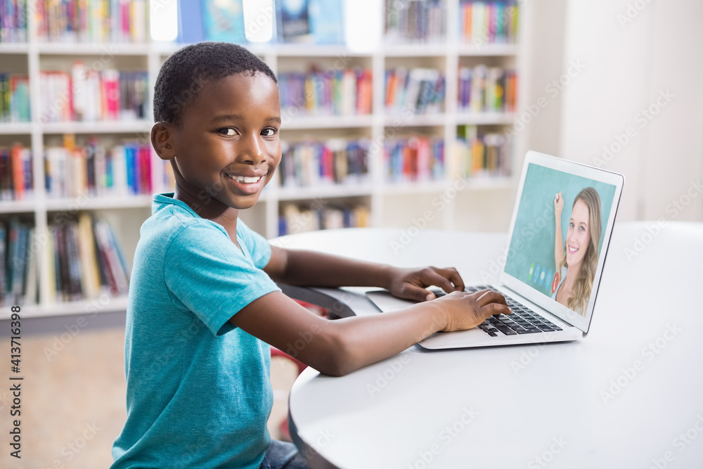 Portrait of male african american student having a video call with female teacher on laptop at libra