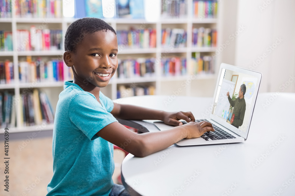 Portrait of male african american student having a video call with male teacher on laptop at library