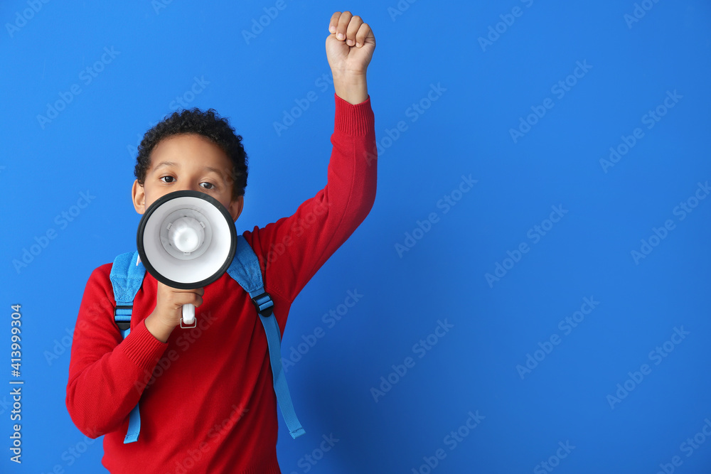 Little African-American schoolboy with megaphone on color background