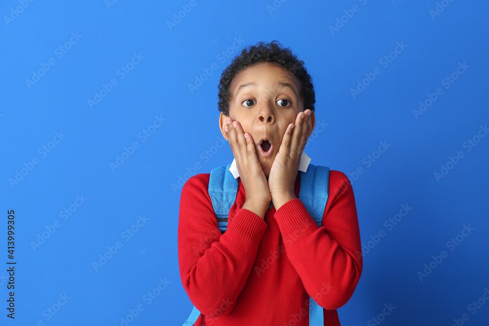 Surprised little African-American schoolboy on color background