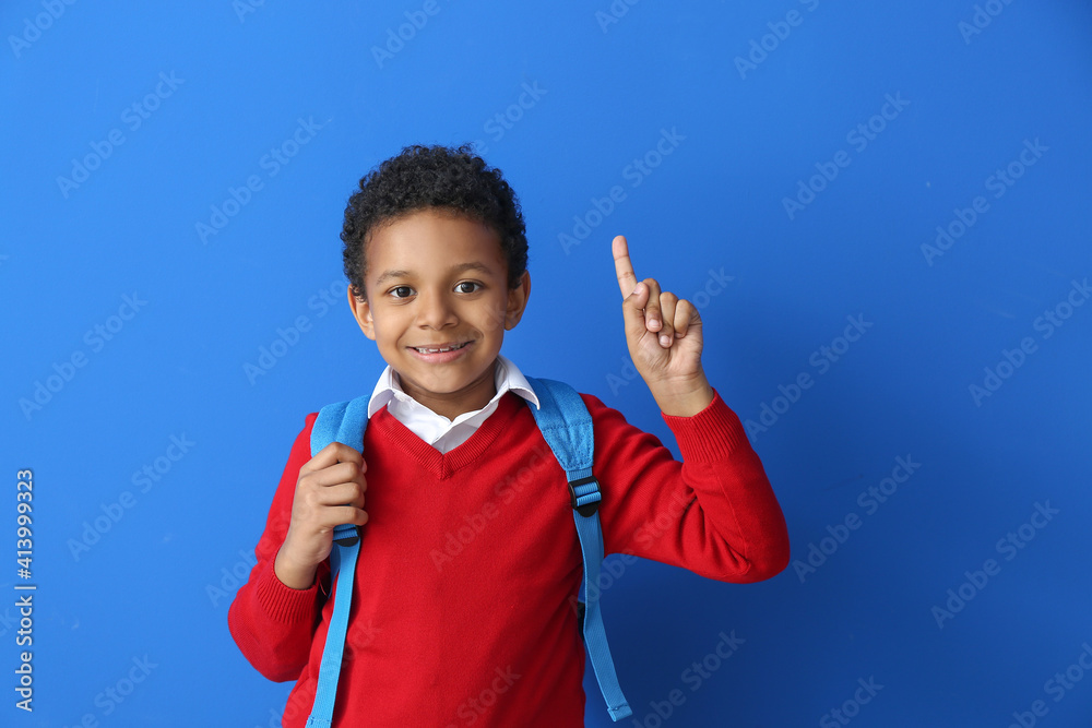 Little African-American schoolboy with raised index finger on color background