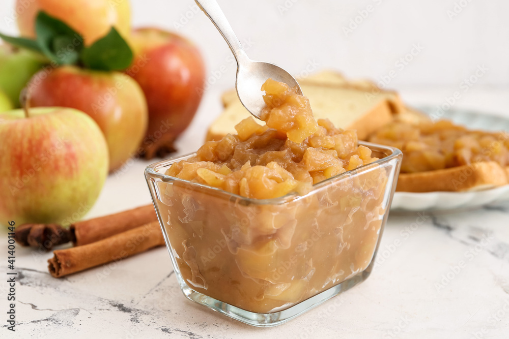 Bowl and spoon with sweet apple jam on light background