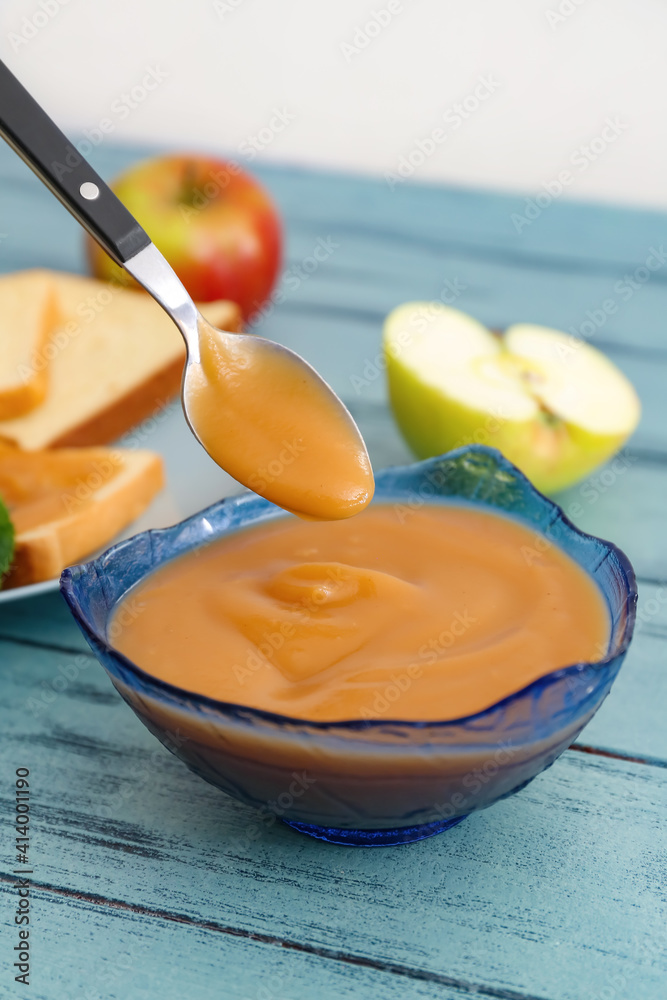 Bowl and spoon with sweet apple jam on color wooden background