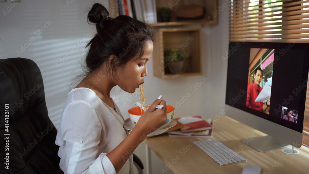 亚洲女性，她在家工作，她正在吃方便面，并与团队视频通话。