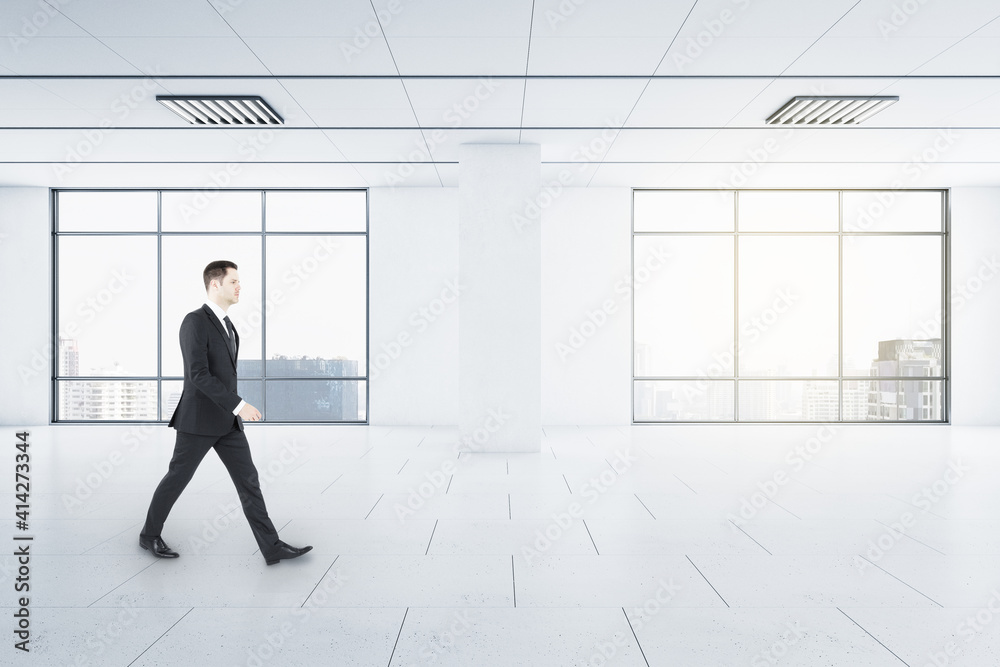 Businessman in motion in light empty spacious hall room with windows and city view