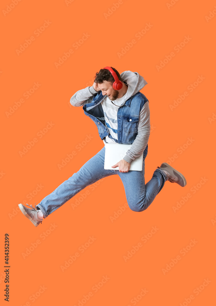 Jumping young man with laptop listening to music on color background