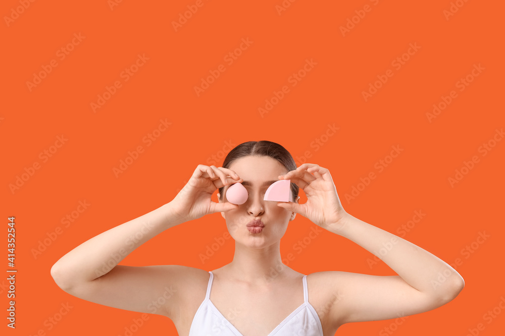 Funny young woman with makeup sponges on color background