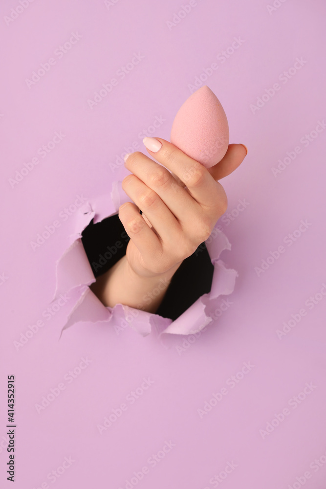 Hand with makeup sponge visible through hole in color paper