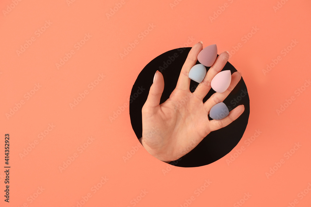 Hand with makeup sponges visible through hole in color paper