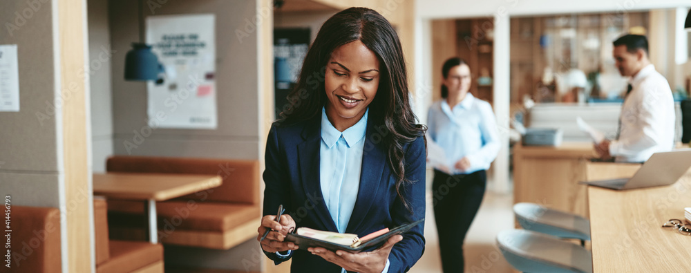 Smiling African American businesswoman walking through an office writing notes