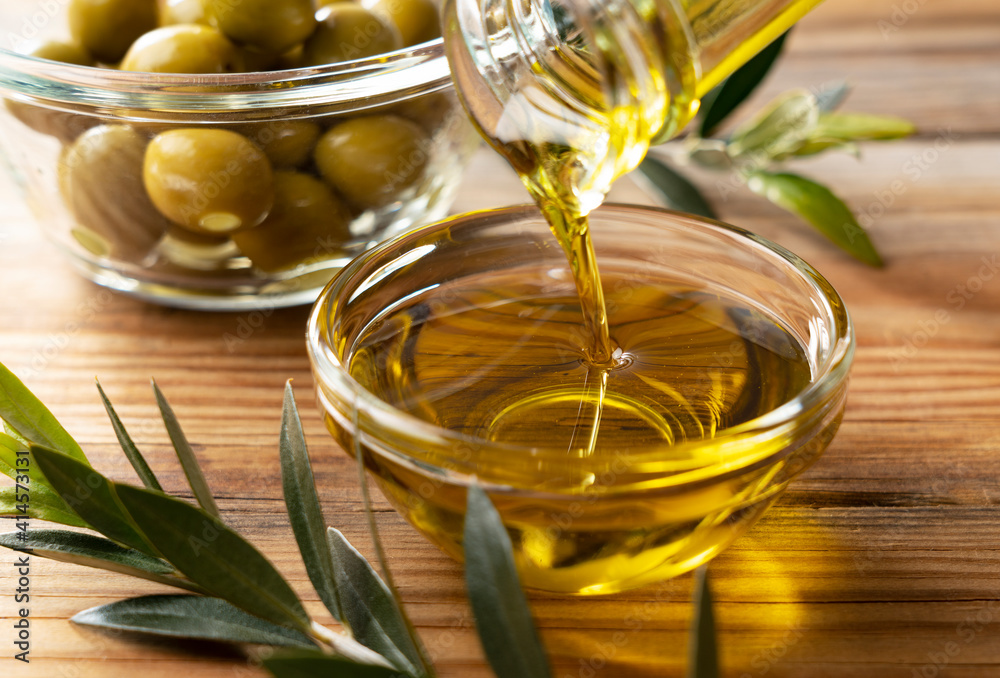 Pour olive oil into a glass bowl set against a wooden background